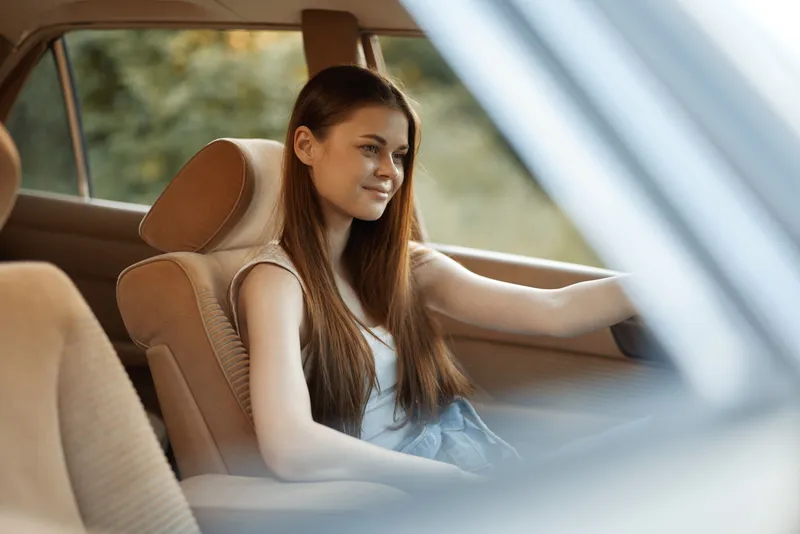 Young woman with long hair enjoying a summer drive in a vintage car, embodying freedom and joy amidst a serene green background.