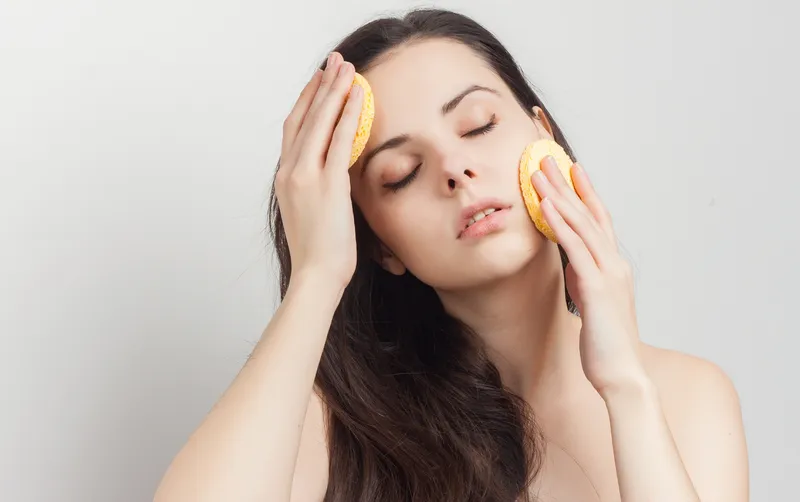 Привлекательная брюнетка с распущенными волосами, обнаженными плечами, спонж возле лица