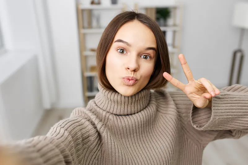 Красивая женщина сидит на диване в квартире, делает селфи на смартфон