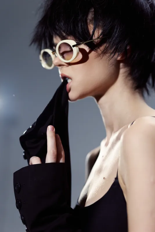 Stylish woman wearing retro sunglasses and black clothing in a moody indoor setting