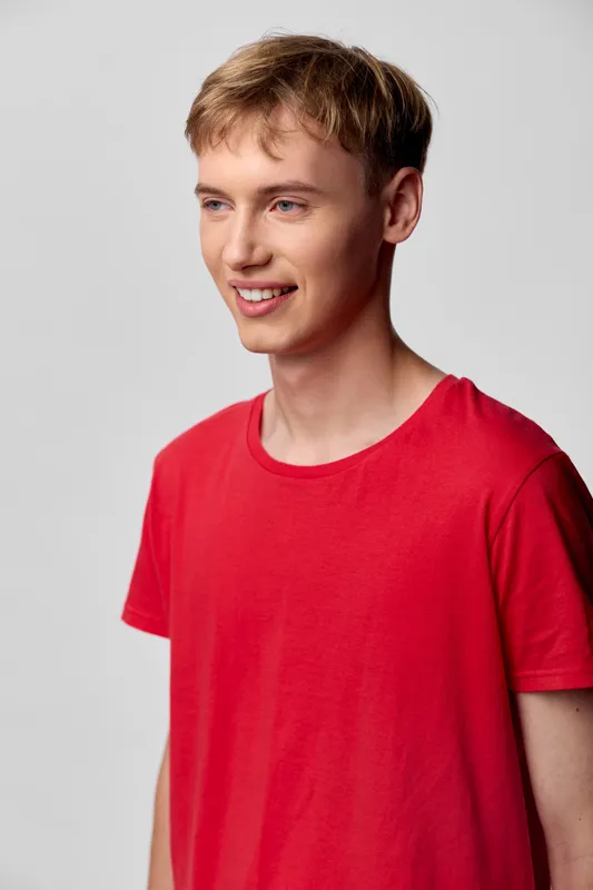 Young man wearing a red casual shirt with a warm smile in a studio setting, bright lighting and relaxed pose against a clean background, conveying approachability and modern style.