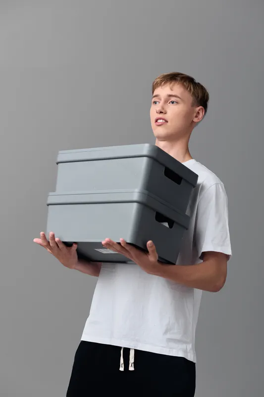 Storage boxes, boy carrying toolboxes, organization and inventory in a clean studio setting, showcasing handling and logistics for product packaging and light warehouse tasks with neutral background