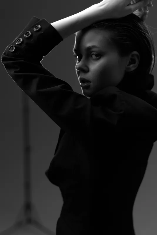 Black and white portrait of a thoughtful woman in elegant black clothing with a moody expression and dramatic lighting.