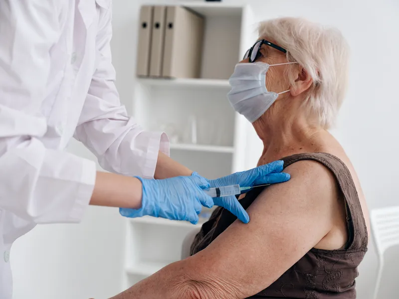 Медсестра делает укол пожилой женщине, вакцинный паспорт