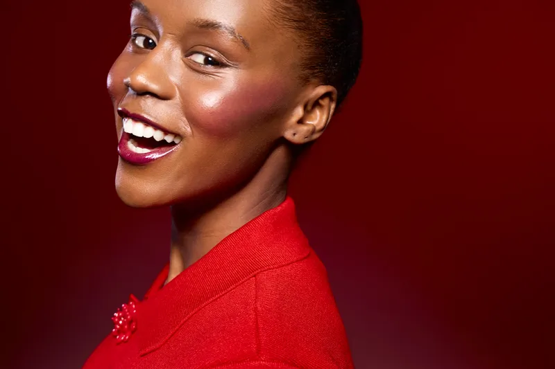 Smiling African American woman with dark skin wearing red clothing looks over shoulder against red background. Concept of beauty, fashion, confidence, and elegant style in portrait photography.