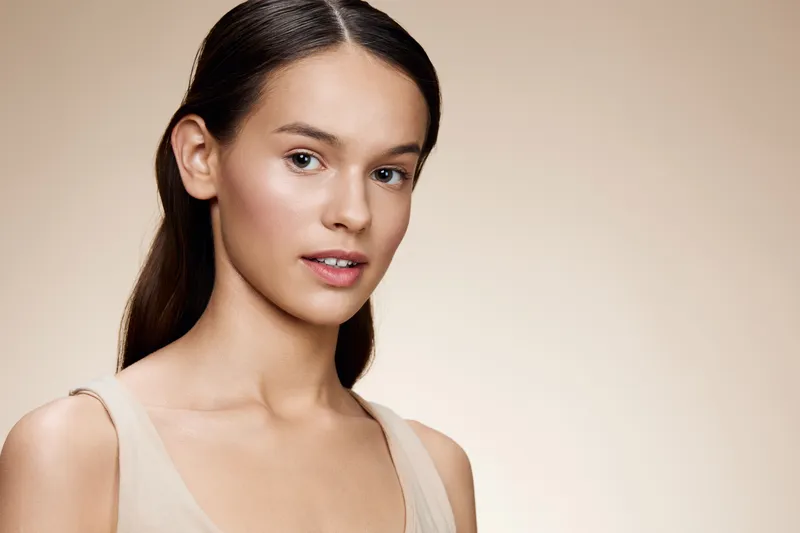 Portrait of a young model with natural beauty, wearing a soft beige top, conveying confidence and elegance against a neutral, warm backdrop
