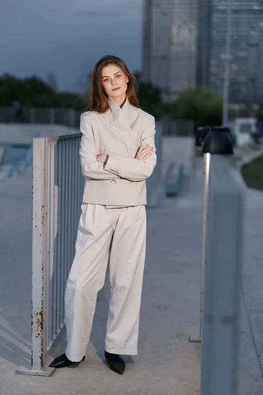 Confident woman in a light grey suit displaying professional elegance in an urban setting, embodying modern business style and empowerment.