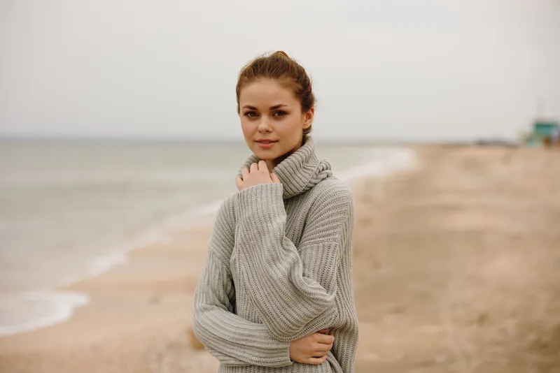Симпатичная женщина в свитере у океана, туризм