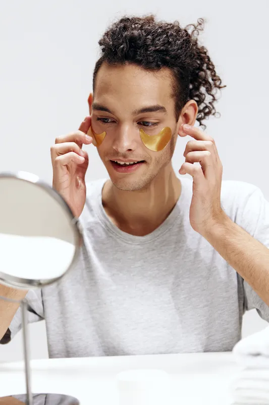 Парень с кудрявыми волосами и патчами на лице касается лица руками, изолированный фон