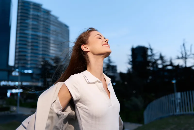 Confident woman enjoying the evening breeze in a modern urban setting, wearing a stylish outfit, embodying success and empowerment in a business context.