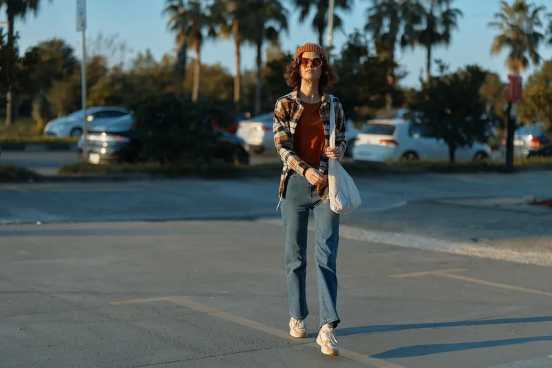 woman walking casual in urban portrait at parking lot, sunlight and golden hour glow, smile and fashion details convey authenticity and candid lifestyle, mindful living and emotional storytelling