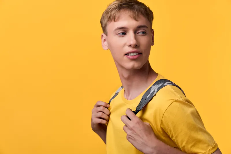 Student with backpack in casualwear against a bright yellow backdrop, showcasing everyday style, readiness for class, and urban exploration in a vivid studio setting and dynamic presence.