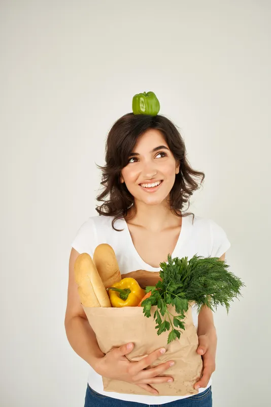 Весёлая женщина в белой футболке с пакетом овощей и продуктов
