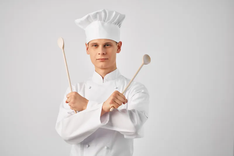 Мужчина в форме шеф-повара на кухне с кухонной утварью, передающий эмоции в ресторане