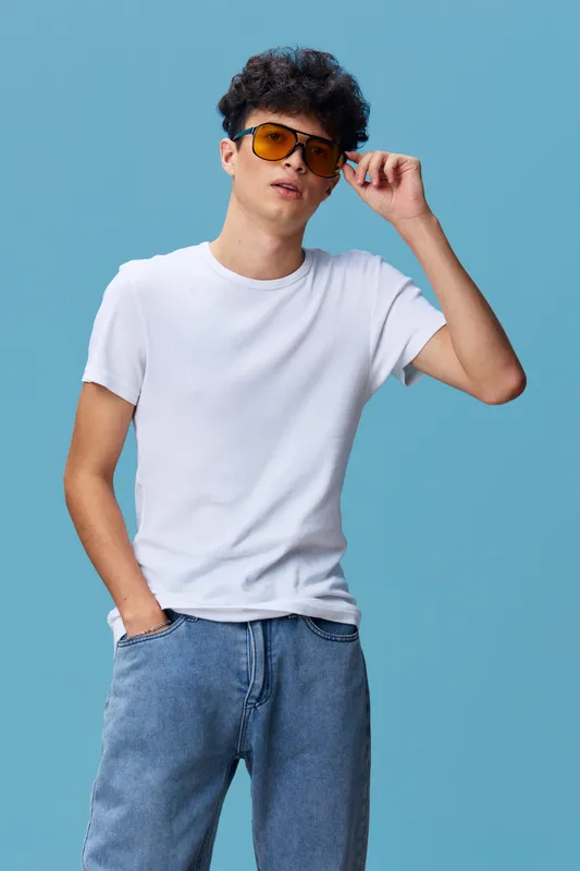 young man wearing white t-shirt and blue jeans poses confidently with sunglasses on blue background, casual style portrait with hand in pocket, modern fashion look