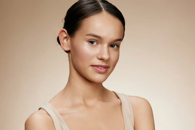Portrait of a young woman with smooth skin, wearing a minimalistic outfit, exuding confidence against a soft beige background Glowing beauty, natural aesthetics, and modern elegance