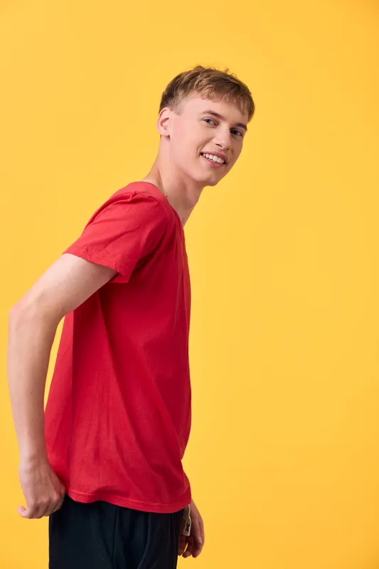 Smiling young man in a red shirt stands against a bright yellow backdrop, casual fashion and upbeat mood, studio lighting highlighting confident posture and friendly vibe