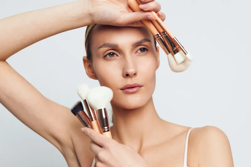 Beauty woman with makeup brushes, portrait view, calm expression, skincare cosmetics concept, soft studio lighting, clean white background, grooming routine, natural glow, smooth skin