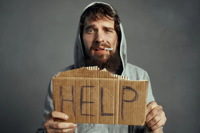 Бедный мужчина с бородой и табличкой с надписью «Help» ведёт образ жизни бродяги