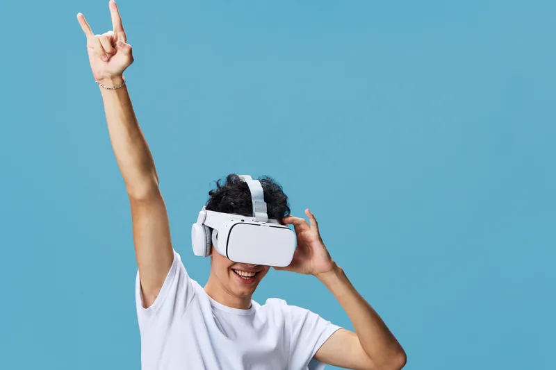 Man wearing virtual reality headset enjoys immersive experience with raised hand gesture, smiling happily against a bright blue background.