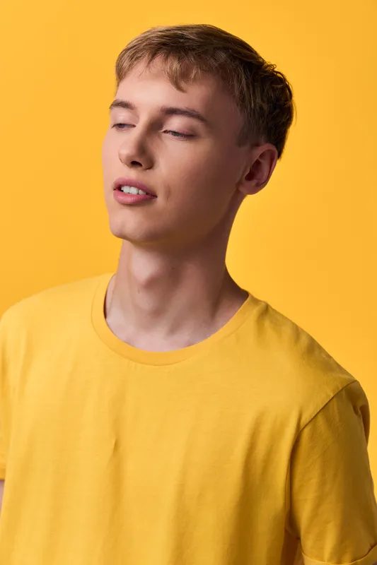 Man in a yellow shirt with closed eyes in a serene studio setting, relaxed mood, soft lighting, casual fashion, calm expression, warm background, minimal composition, lifestyle vibe