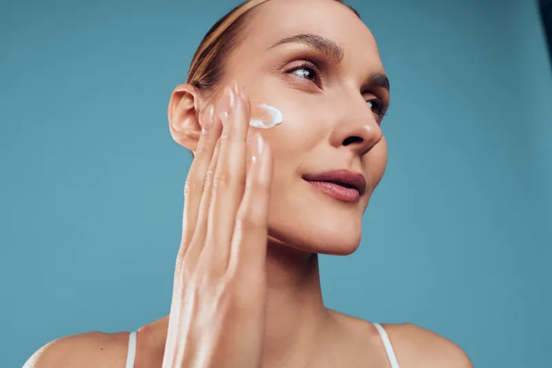 Woman applies moisturizer cream to her face during skincare routine, beauty and spa mood, health and hygiene care for smooth skin, natural glow, soft copyspace