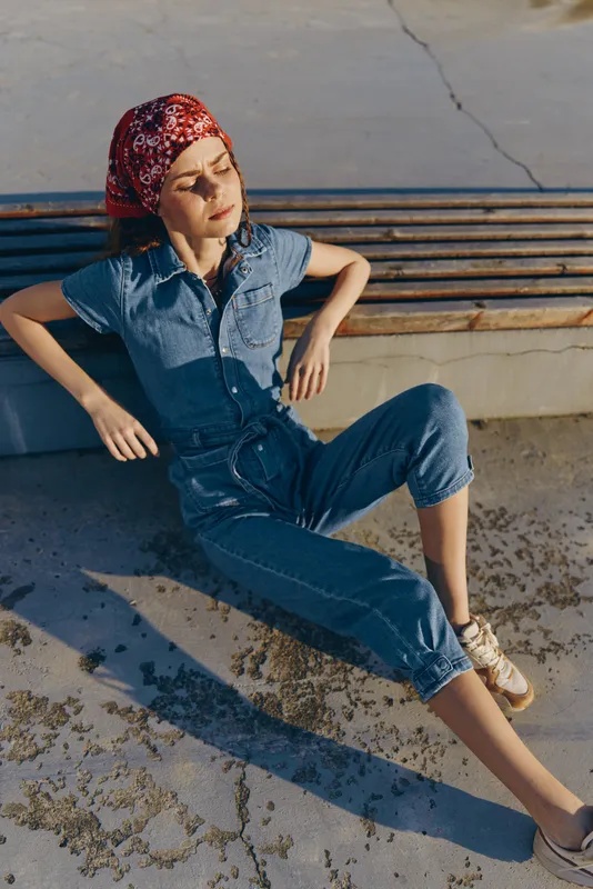 Lifestyle woman in modern boho-western denim street style relaxing outdoors with casual pose and film color tones, enjoying sunny day and creative fashion vibe.