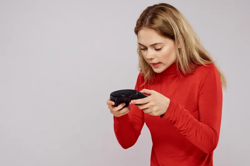 Женщина с геймпадом в руках, играющая в игры, эмоции, образ жизни, досуг, красная рубашка, светлый фон