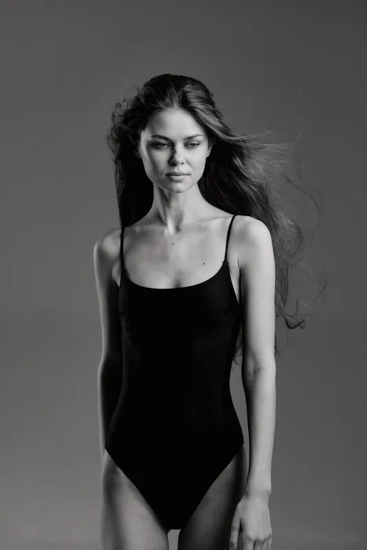 Black and white portrait of a slender woman in black bodysuit with flowing hair and calm expression