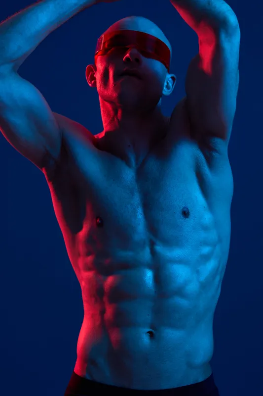 Muscular man creating dynamic poses with colorful lighting. This vibrant black and white image showcases strength and intense emotion.