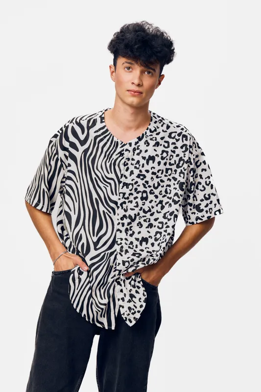 young man wearing a black and white animal print shirt and black pants stands confidently against a plain white background, showcasing unique casual style.