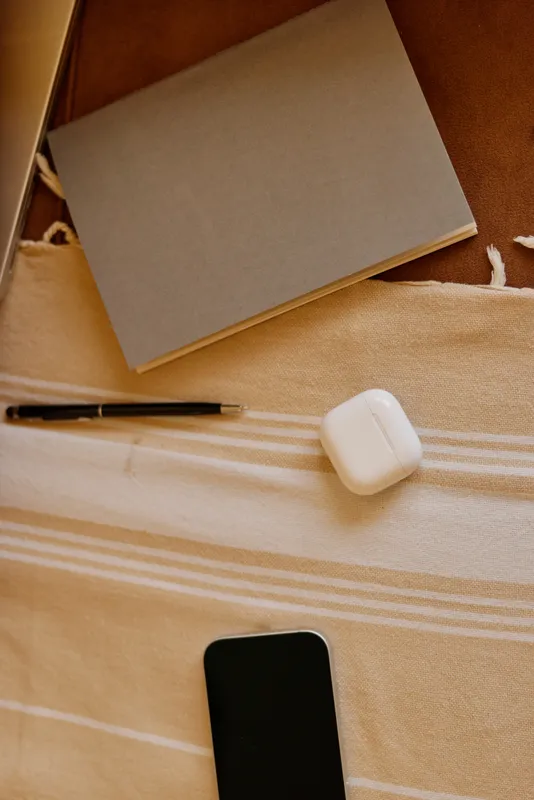 Cozy home workspace scene with a notebook, pen, earphones case and smartphone on a striped bedspread, suggesting casual daily planning and relaxed routine