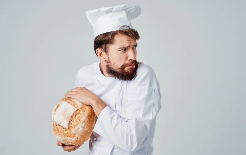 Мужчина-повар на кухне, работа с хлебобулочными изделиями на светлом фоне