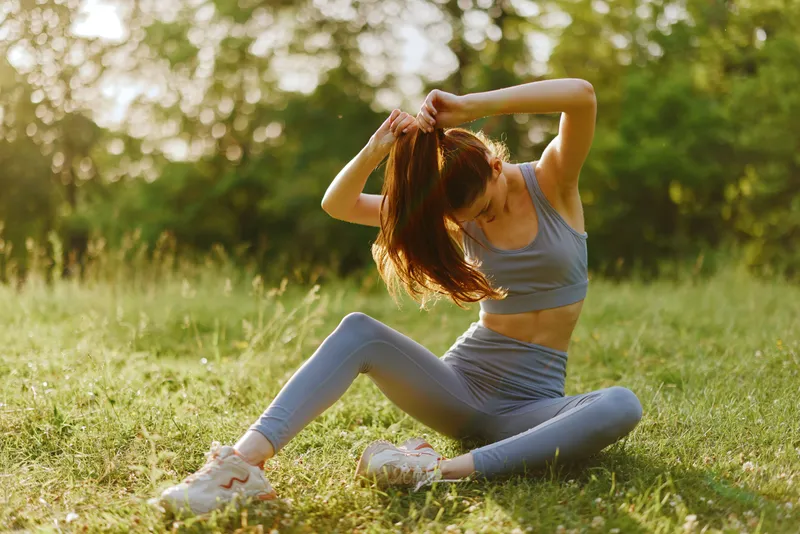 Young woman exercising outdoors in sporty attire, showcasing a healthy lifestyle and joyful emotions in a natural green setting