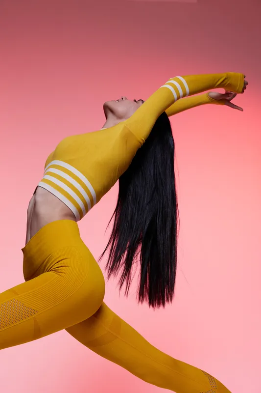 Woman sport fitness stretching in vibrant yellow activewear, showing flexibility and strength against a pink studio backdrop, emphasizing health and movement.