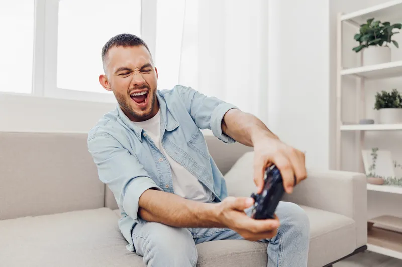 Dynamic man enjoying gaming experience, showing excitement and joy while playing video games in a cozy living room setting. Perfect for lifestyle themes in 2025.