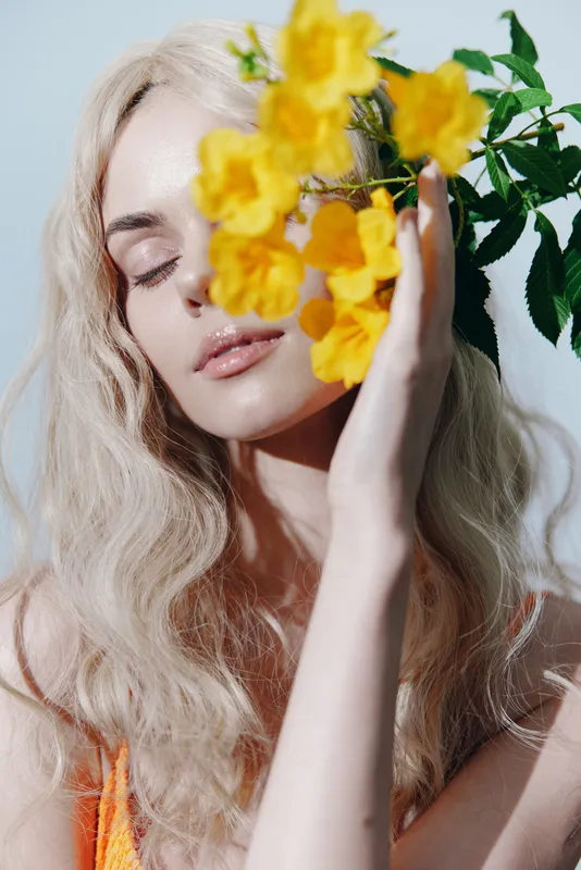 Молодая женщина с blond-волосами нежно держит ярко-желтые цветы, демонстрируя красоту и безмятежность