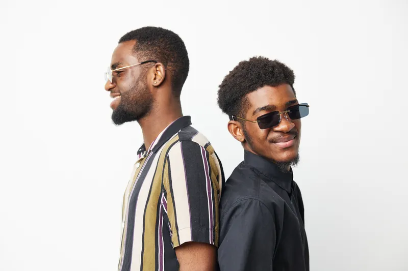 Two stylish black men with sunglasses, showcasing their unique fashion sense and confidence. The image reflects modern urban life and youthful energy.