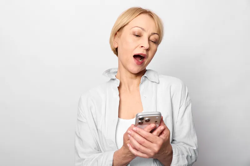 Woman smartphone surprised shocked expression, female portrait indoors on white background, holding mobile phone, reading message, open mouth, communication