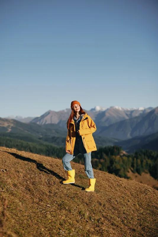 Женщина в полный рост идет по холму осенью и смотрит на горы