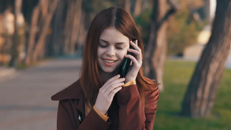 Симпатичная женщина в пальто с телефоном в руке прогуливается по парку и отдыхает