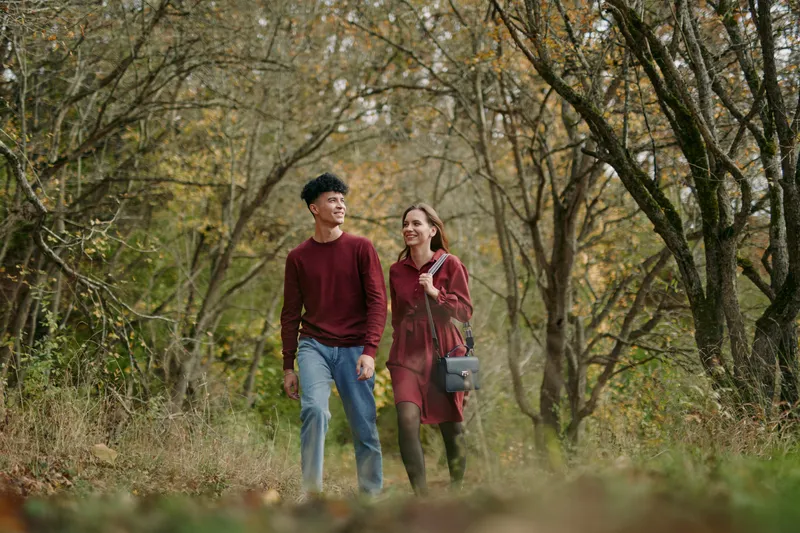 Authentic candid moment of two friends walking along a woodland path, natural light, unposed posture, genuine connection, casual outfits, calm mood, everyday realism.