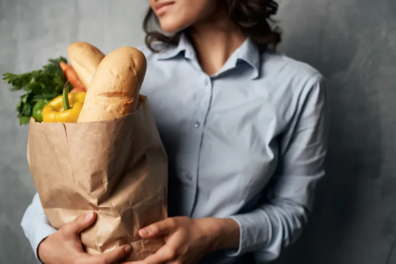 Симпатичная женщина в голубой рубашке с пакетом продуктов в супермаркете