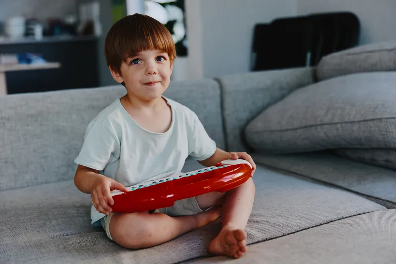 Happy boy playing music with a red toy keyboard in a cozy living room. Joyful atmosphere fills the space, enhancing the playful scene.