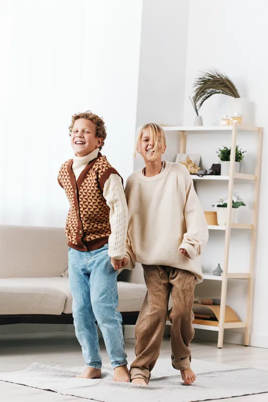 Authentic playful scene highlights school themed lifestyle with two children sharing a joyful moment indoors, wearing cozy outfits, movement, laughter, and genuine connection.
