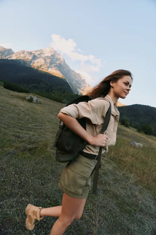 A young woman hiking through a rugged mountain meadow with a backpack, she faces the wind and keeps a steady pace, intent on the journey ahead.