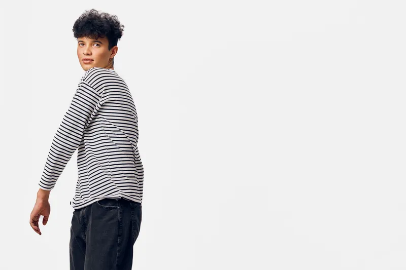 Young man in striped long sleeve shirt looking back over shoulder with neutral expression, casual clothing, isolated on white background.