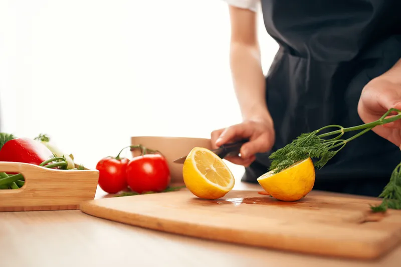 Шеф-повар держит в руках нож и нарезает овощи и лимон на кухне
