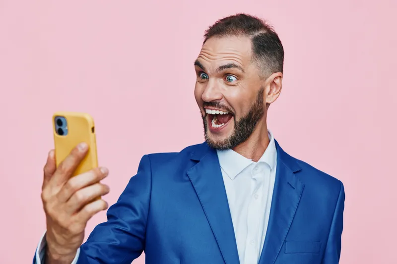 A confident business professional poses against a vibrant pink background, capturing excitement and optimism as he takes a selfie, showcasing ready-to-act charisma and dynamic leadership.