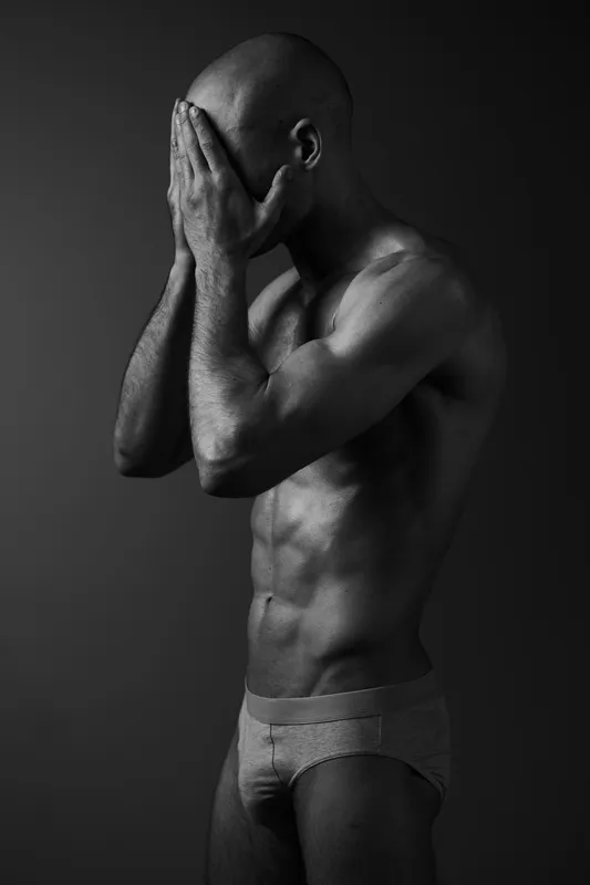 A pensive man expressing deep emotions while partially covering his face, captured in striking black and white tones, showcasing the mood of introspection and vulnerability.